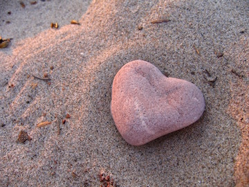 A heart shaped rock sitting in the sand. 